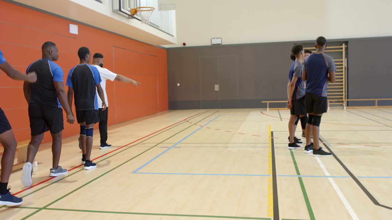 Colegas de equipe masculinos diversos seguindo o treinador apontando, andando na academia sobre linhas pintadas e se unindo para um exercício.