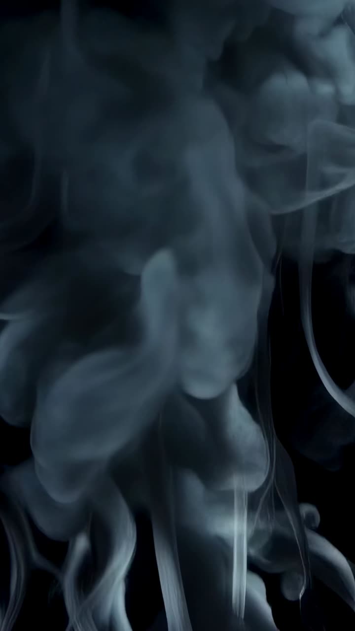 Video verticale: pennacchio verticale bluastro di fumo che si arriccia e sale su un set nero leggermente illuminato