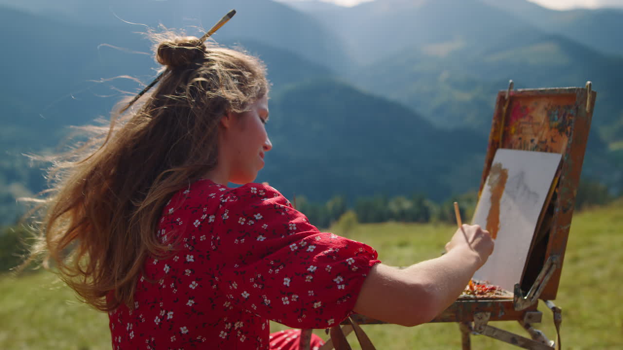Woman painter drawing mountains landscape on meadow. Girl painting using easel.