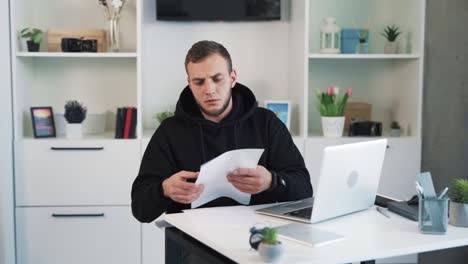 El-Hombre-Está-Sentado-En-Su-Escritorio-En-La-Oficina,-Mirando-Algunos-Papeles-Con-Insatisfacción,-Y-Luego-Arruga-Algunas-Hojas-Y-Las-Tira-A-Un-Lado