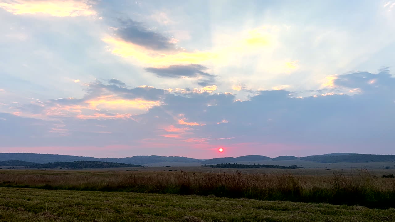 Timelapse, cloudy sunset over vast grassland with fiery sky on fire