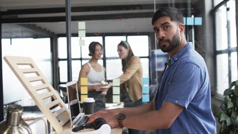 Young-Asian-man-stands-by-his-laptop-in-modern-business-office-setting