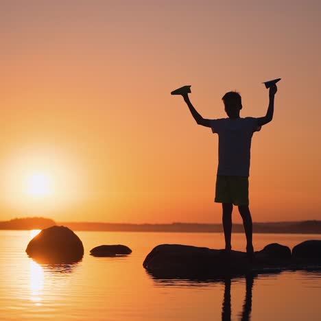 a happy child is playing with a paper airplane at sunset. classes with children outdoors. lifestyle