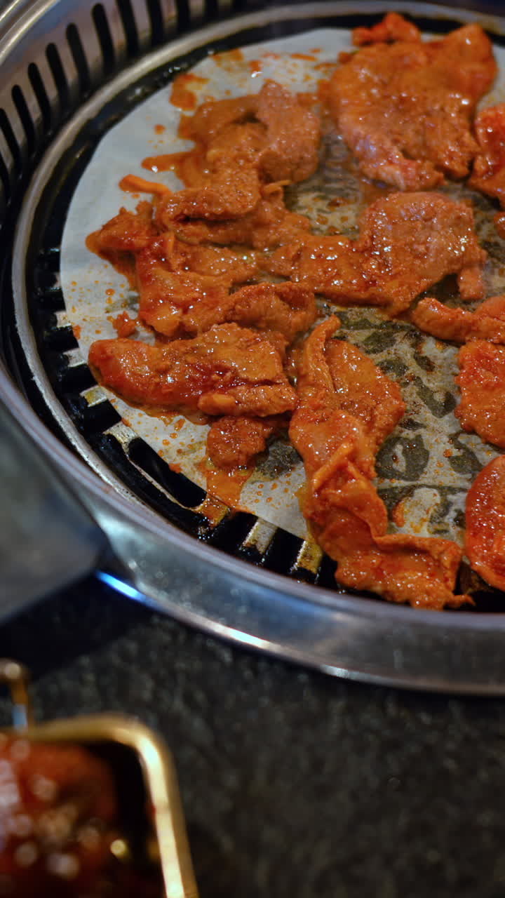 Man putting French fries on a table near multiple pieces of meat cooking at a restaurant in Copenhagen, Denmark. Vertical