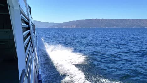 view from side of boat or ship speeding towards island in the distance on the ocean with the surf and spray splashing from the sides