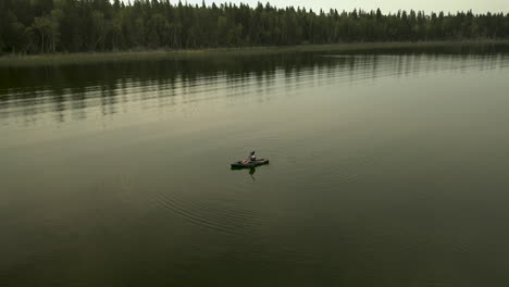 un hombre en kayak en un gran lago templado, pinos en el fondo