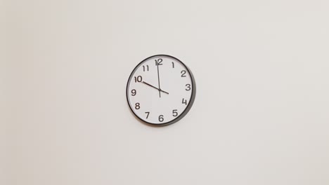 a wide 4k shot of a classic black and white wall clock on a plain white wall, displaying the time as 10:00.
