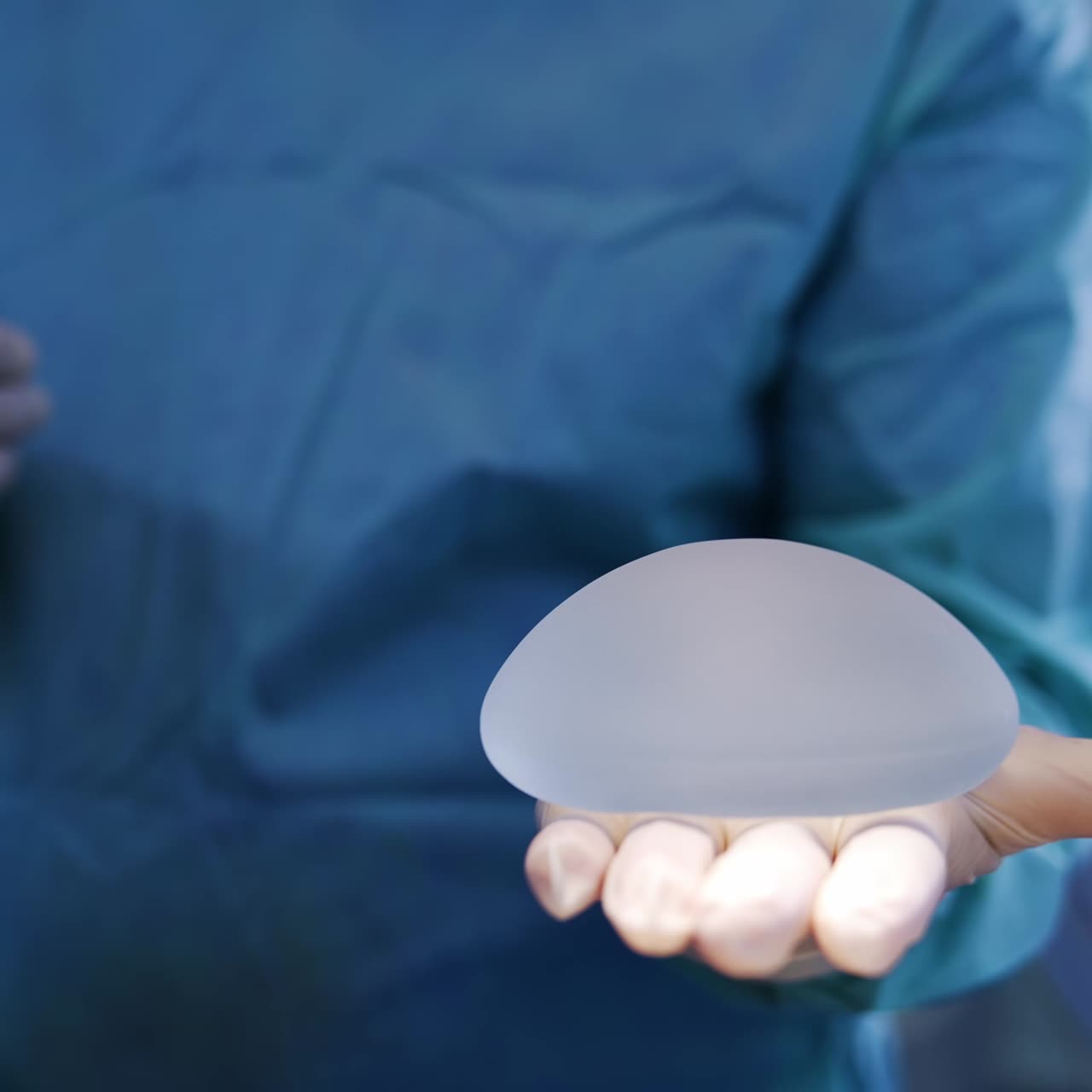 Unrecognized doctor holding a breast implant on his palm. Surgeon demonstrating the material turning it on his hand. Close up