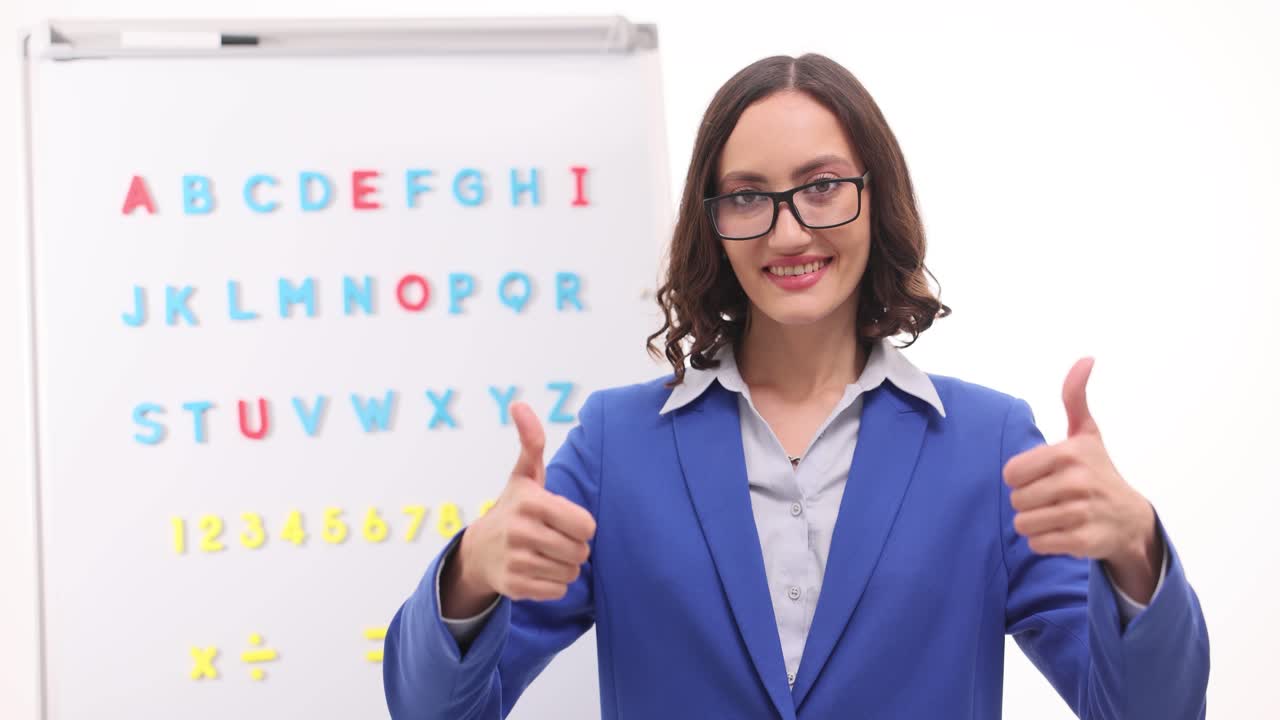 Smiling Woman Teacher Giving Thumbs Up in Front of Alphabet Whiteboard