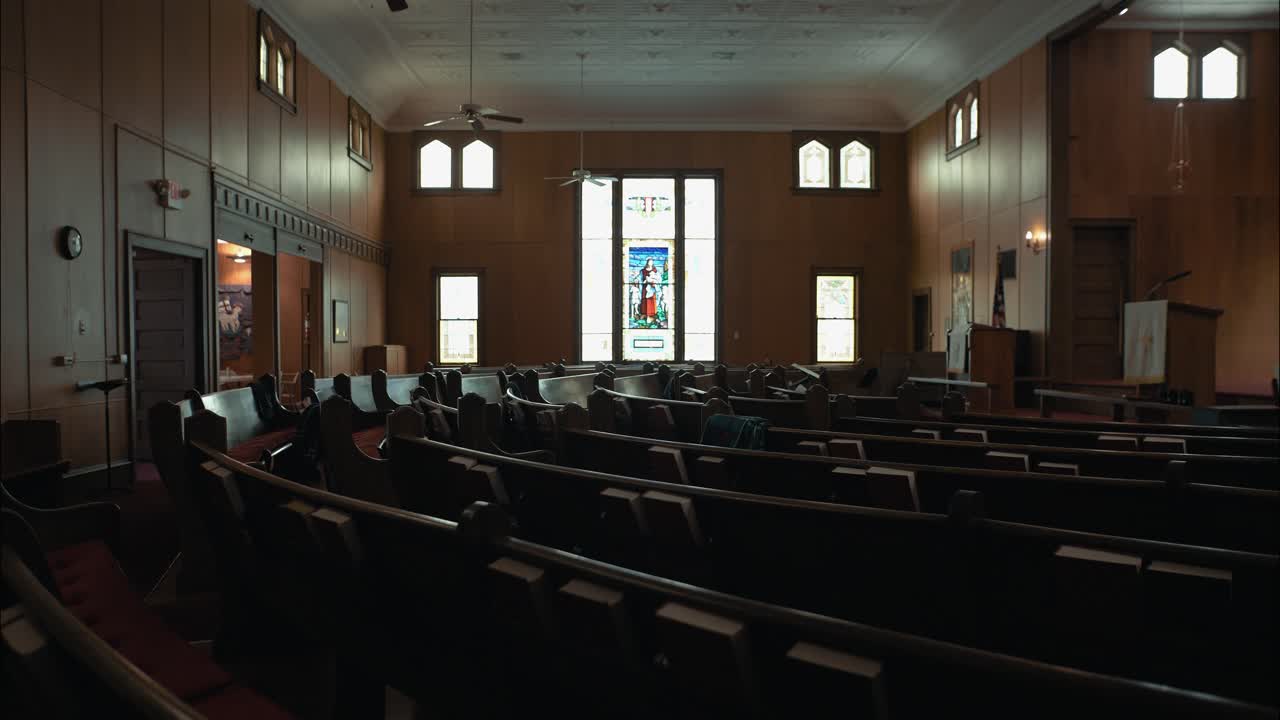 Wide shot of empty church pews facing a stained-glass window, capturing the calm and sacred atmosphere of a traditional worship space