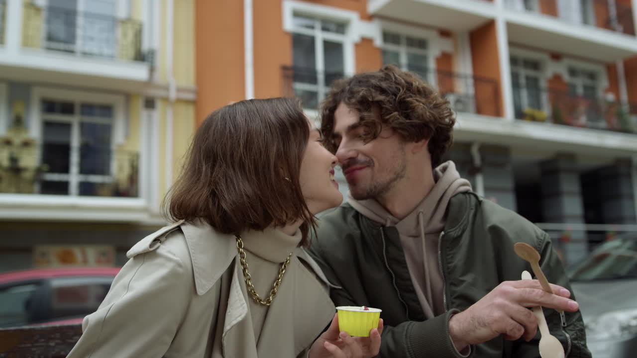 Coppia allegra che mangia un gelato all'aperto. Coppia gioiosa che si bacia in una strada cittadina.