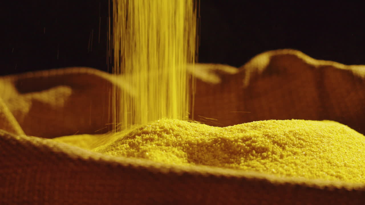 Close-up of golden cornmeal or polenta being poured into a textured sack, with a wooden spoon in the pile