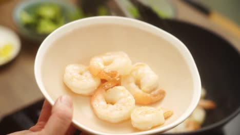 unrecognizable person putting fried prawns from pan into bowl