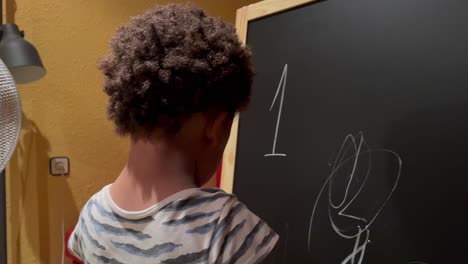 adorable y exótico niño afroamericano de dos años haciendo sus primeros dibujos con una tiza en una pizarra en casa