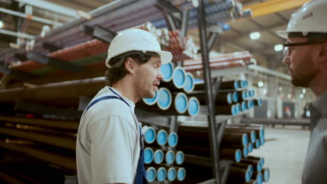 factory worker telling engineer about metal pipes in industrial warehouse