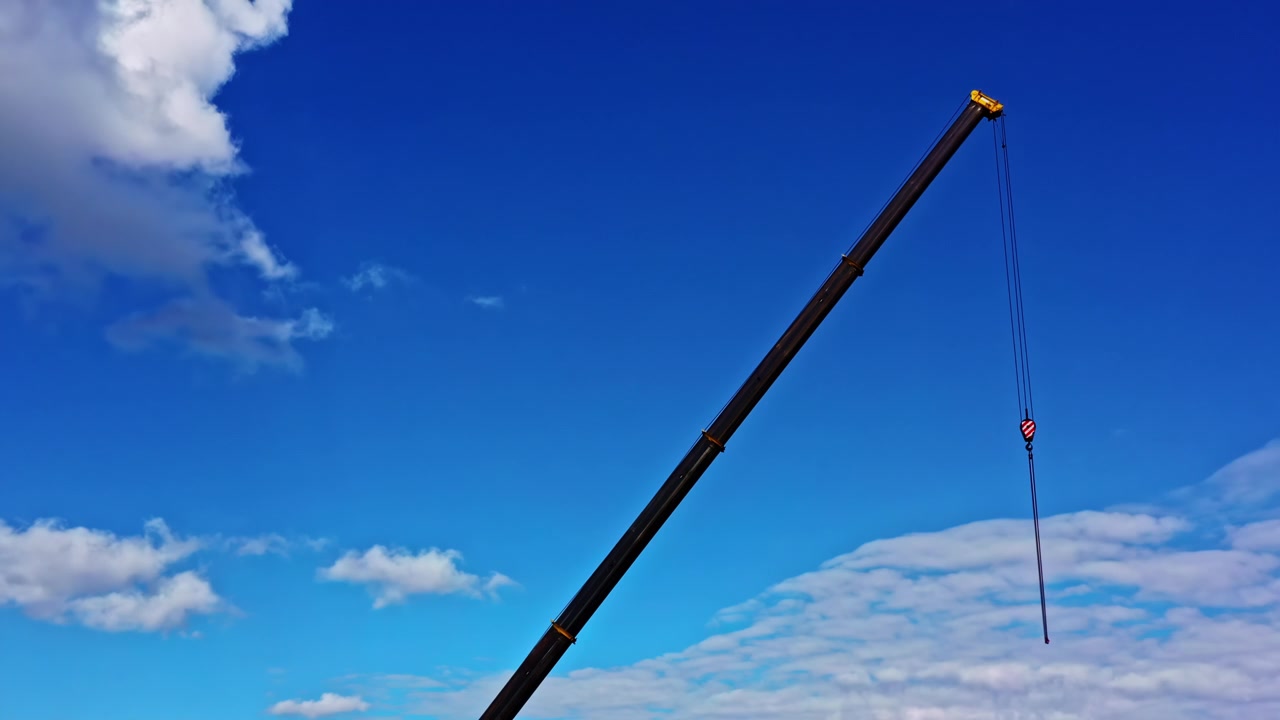 Lança de guindaste de construção com um gancho estendendo-se para um céu azul vívido com nuvens brancas fofas.