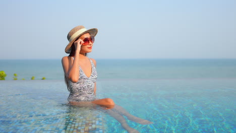 Charming-Asian-woman-sitting-in-infinity-pool-water-contemplating-panorama