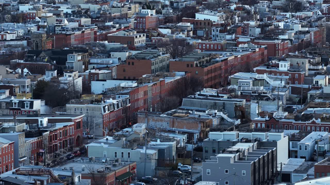 Luftfoto af et tæt bebygget rækkehuskvarter i Baltimore om vinteren, der viser rækker af murstenshuse, flade tage, smalle gader og byens boligarkitektur under koldt sæsonbetonet lys. Vidvinkelbillede.