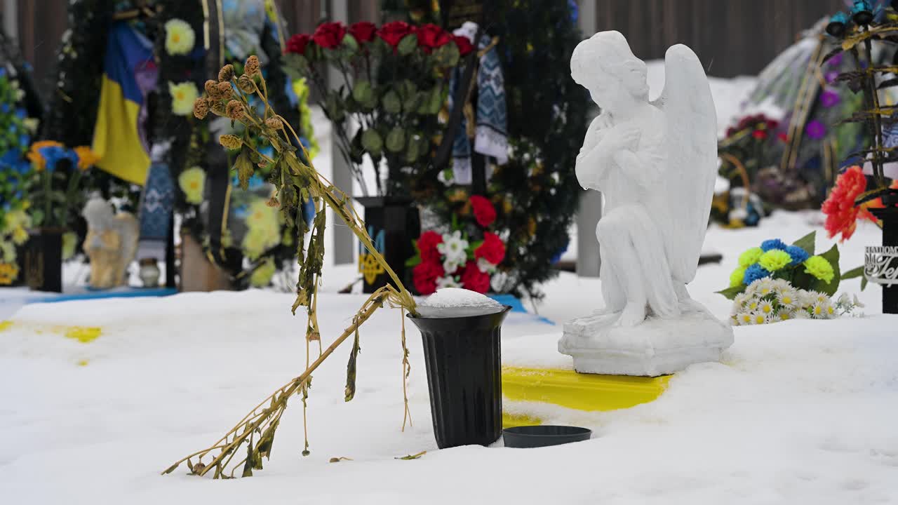 A wilted bouquet of flowers sits by an angel statue at Irpin Cemetery, Ukraine, on a winter day, honoring a fallen Ukrainian soldier from the Ukraine-Russia war.