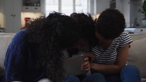 Mixed-race-lesbian-couple-and-daughter-using-digital-tablet-on-couch-laughing