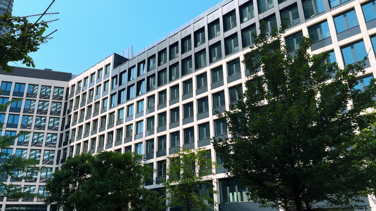 Green landscaped office building. A contemporary office building showcases large windows, framed by vibrant green trees during a sunny day