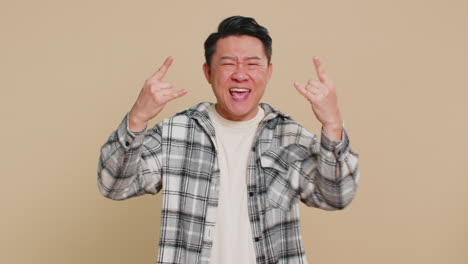 행복한 아시아 남자가 록 앤 롤 제스처를 보여주는 냉정한 손으로 신호 미친 표정 춤추는 승리 승리