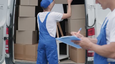 two young workers of removal company are loading boxes and furniture into a minibus