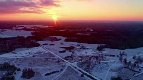 aerial drone view of a snow-covered landscape with the sun setting orange on the horizon