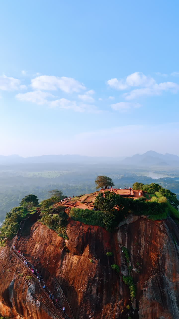 Brown mountain with stairs to the top and lush greenery on top. Aerial view on Sigiriya Fortress ruins. Hazy scenery at backdrop. Vertical video.