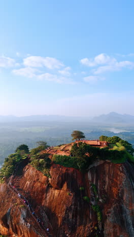 brown mountain with stairs to the top and lush greenery on top. aerial view on sigiriya fortress ruins. hazy scenery at backdrop. vertical video.