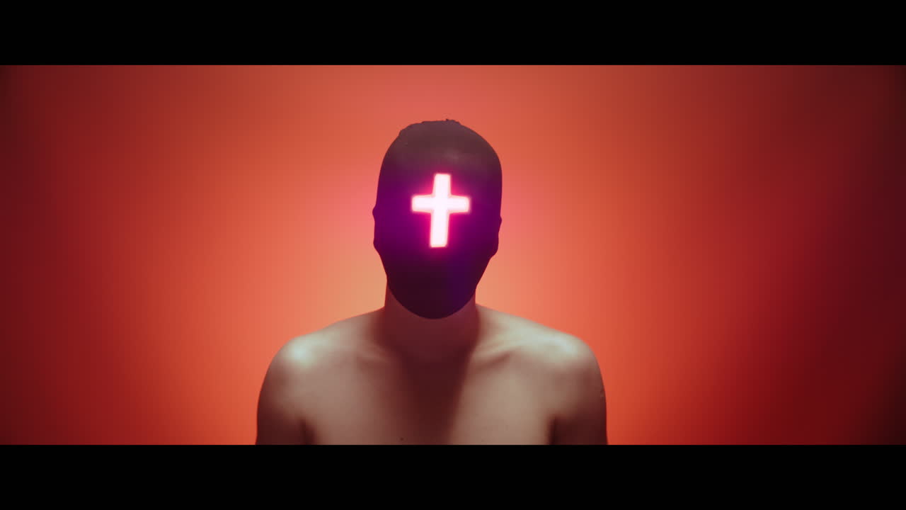 Masked man with cross of light glowing on his face nods