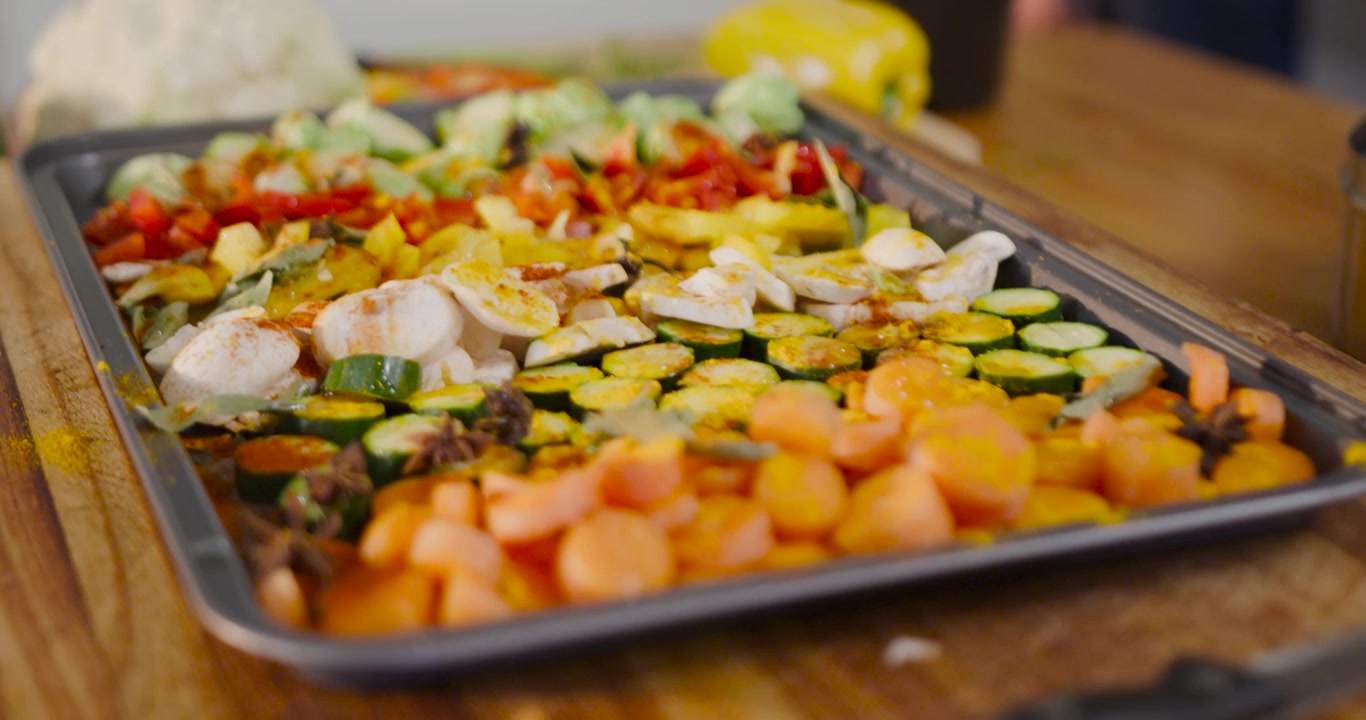 Camera shifting focus and angle to reveal roasting tray holding seasoned vegetables on wooden board