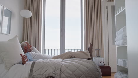 tourist man jumping on hotel bed resting after successful travel journey enjoying retirement vacation