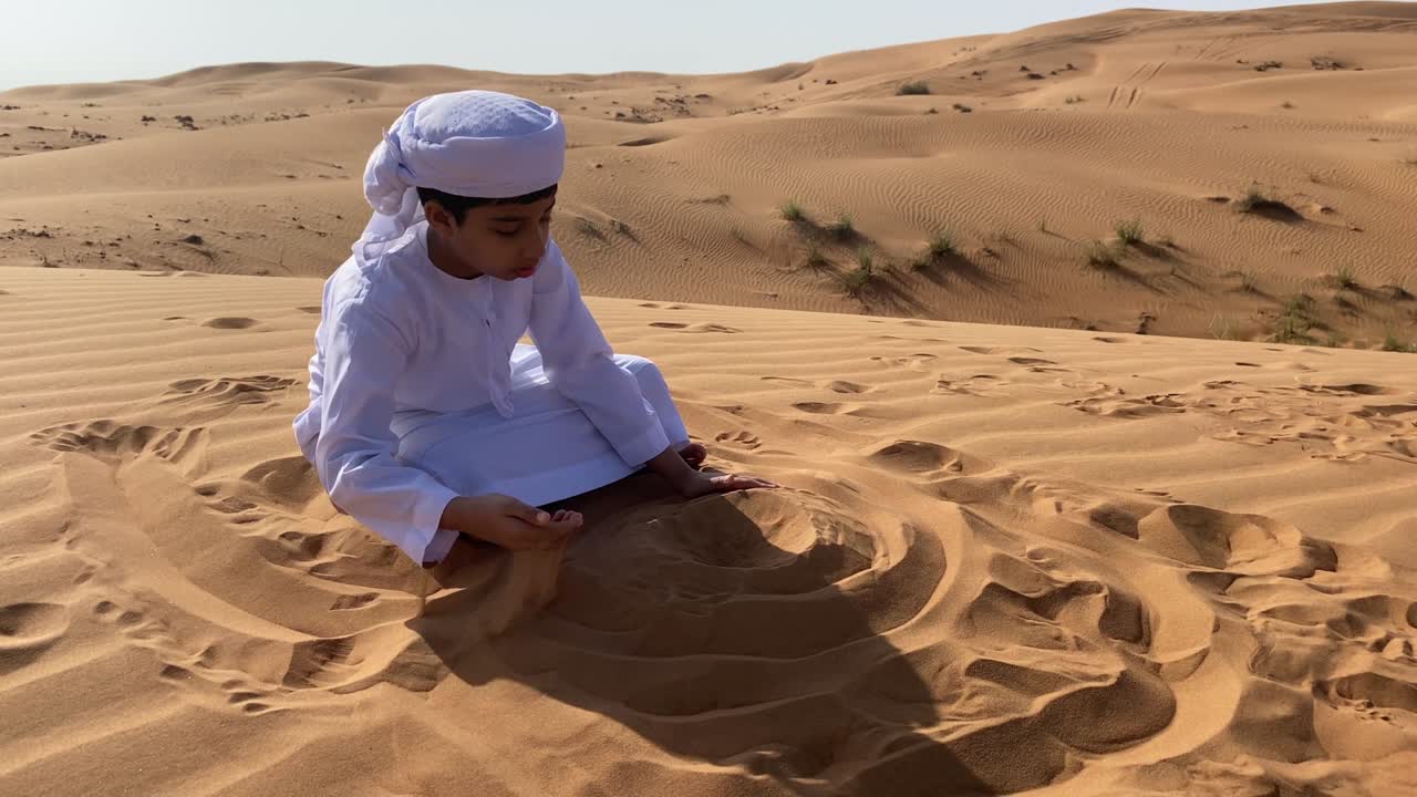 Emiratisk barn leger med sand i ørkenen