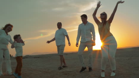 Gran-Familia-Feliz-Bailando-En-La-Playa-Al-Atardecer