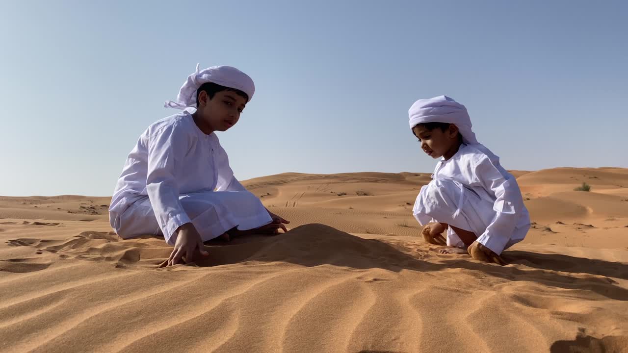 To emiratiske børn leger med sand i ørkenen.