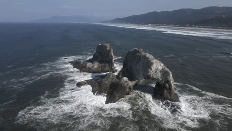 white foamy waves lap up against twin rocks off the oregon coast, aerial orbit