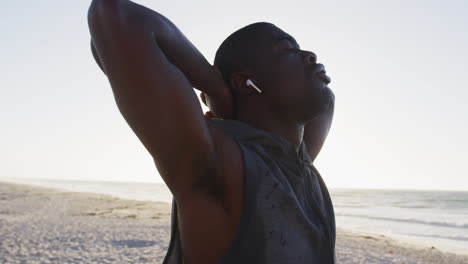 hombre afroamericano enfocado estirándose con los ojos cerrados, haciendo ejercicio al aire libre en la orilla del mar