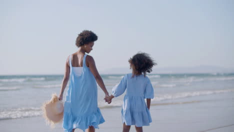 happy woman and daughter walking along beach, holding hands and talking together