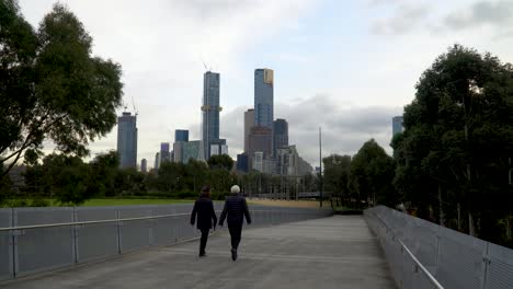 a couple walk down a melbourne walkway with the skyline in the background - exercise during the coronavirus lockdown