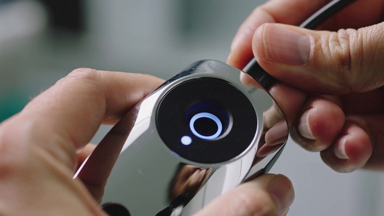 Bringing plug, right hand inserting cable into chrome device with glowing ring at bench to charge