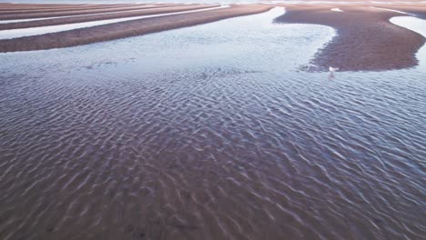 Rising-reveal-over-rippling-sea-water-and-golden-sandy-dunes-with-blue-sky