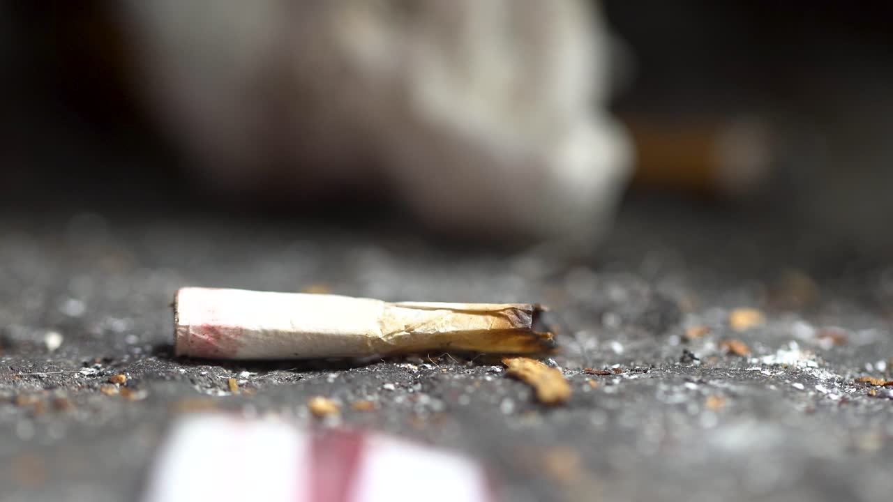 tiro macro 4k de colilla de cigarrillo con lápiz labial rojo en el suelo