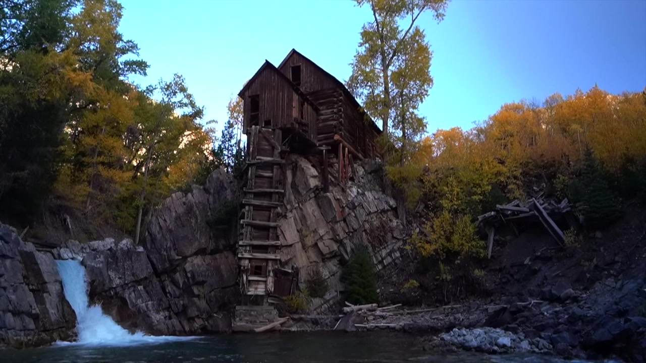 Solnedgang i skumringen ved The Crystal Mill, en gammel sølvmine, klippefremspring, kraftværk og træbygning, et vartegn i Marble, Colorado. Efterårsfarver, blå himmel, landskab med Crystal River-vandfald og flodbund