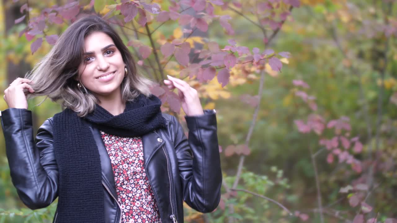 Brunette i høstskog står nær gule og røde blader og smiler inn i kameraet.
