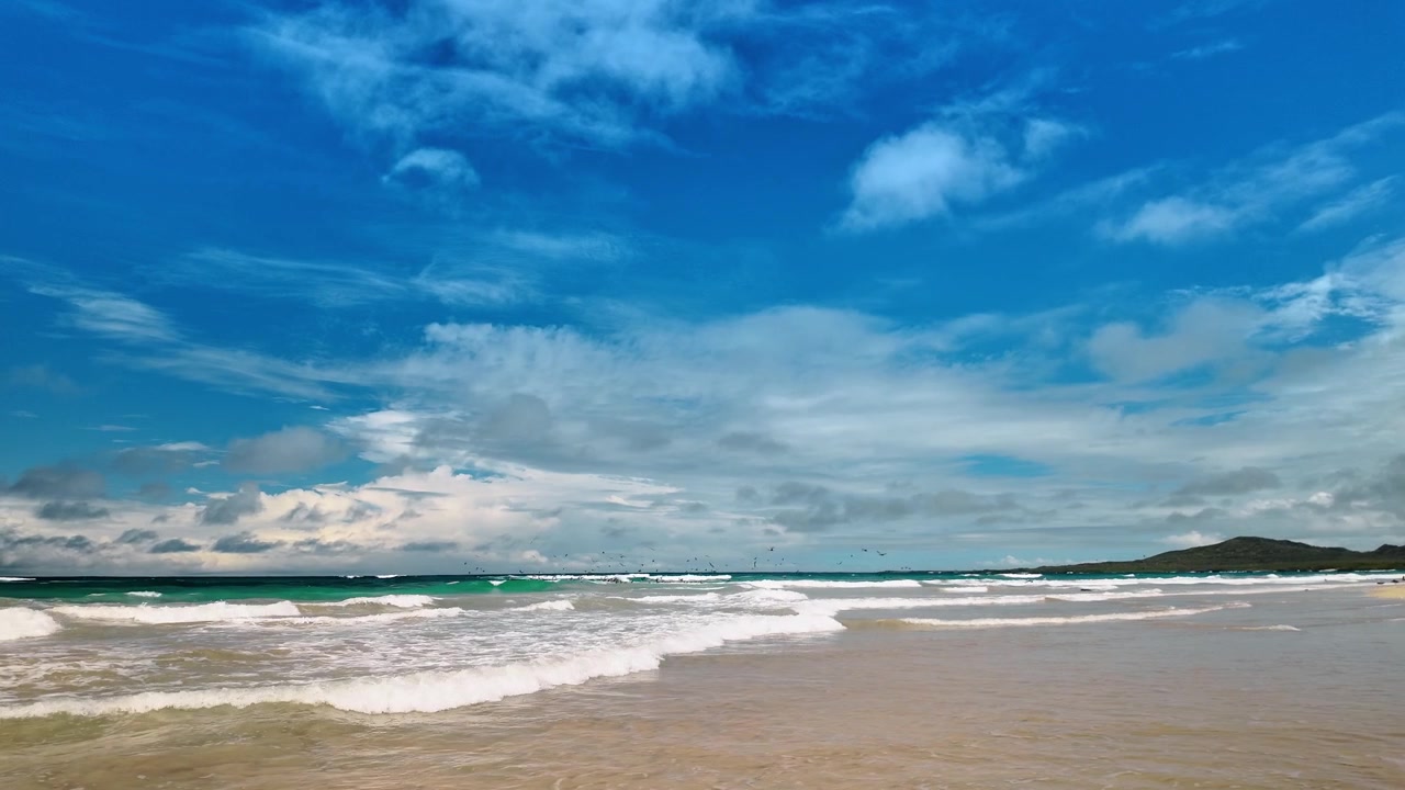 Vista panoramica della costa oceanica sull'isola Isabela, Galapagos. Ampio paesaggio di spiaggia sabbiosa vuota e onde turchesi che si infrangono sotto un cielo blu nuvoloso