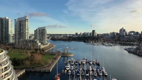 multiple pleasure yachts moored at scaffoldings at each sides of the false creek inlet in downtown vancouver between high buildings on a cloudy day