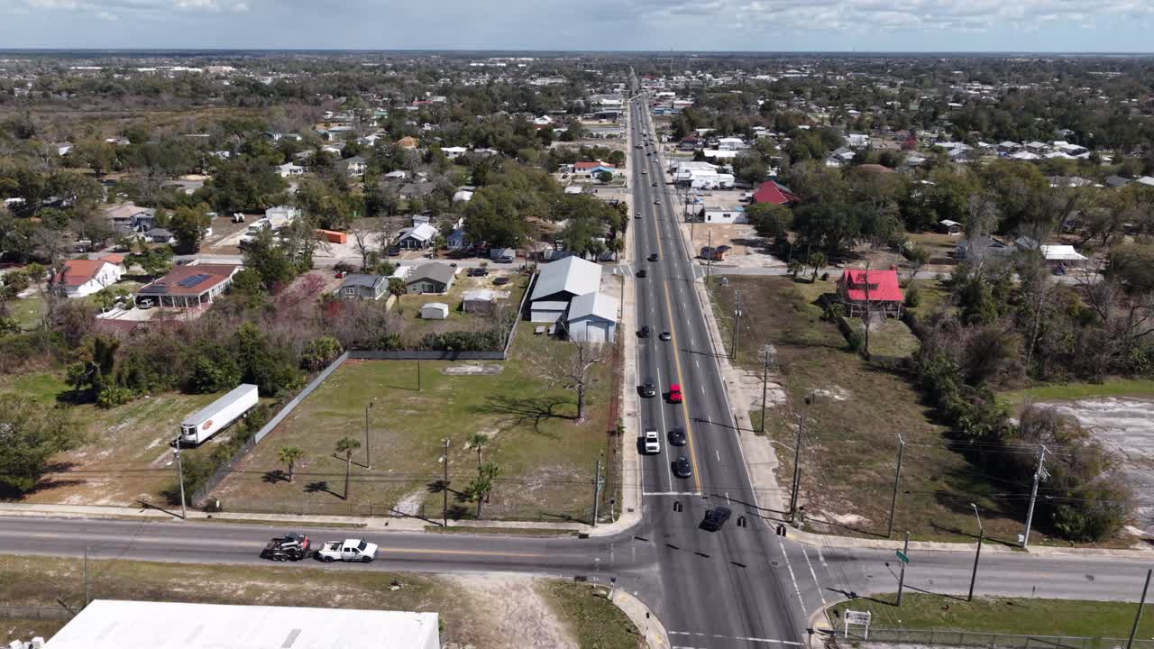Orbita del drone sopra una lunga autostrada rettilinea che attraversa un quartiere residenziale suburbano con case e traffico, 30A, Florida, USA.