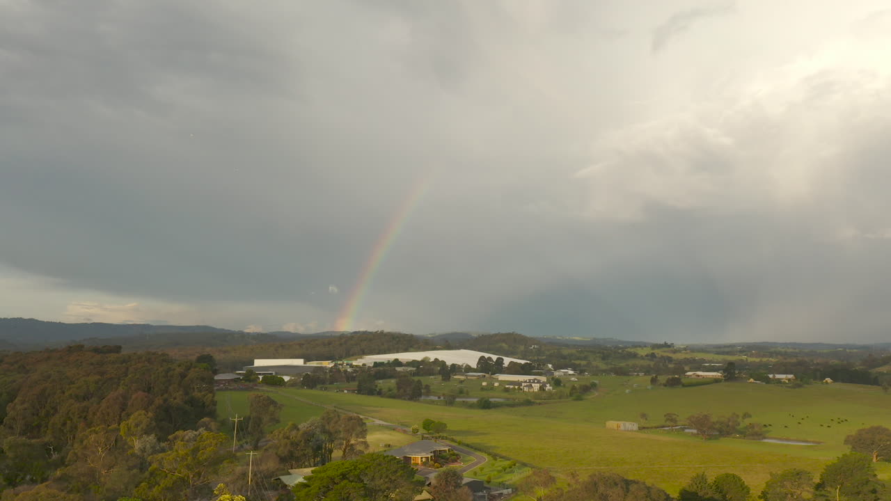 cámara empujando suavemente hacia adelante a través de un paisaje natural sereno, revelando un arco iris en el cielo