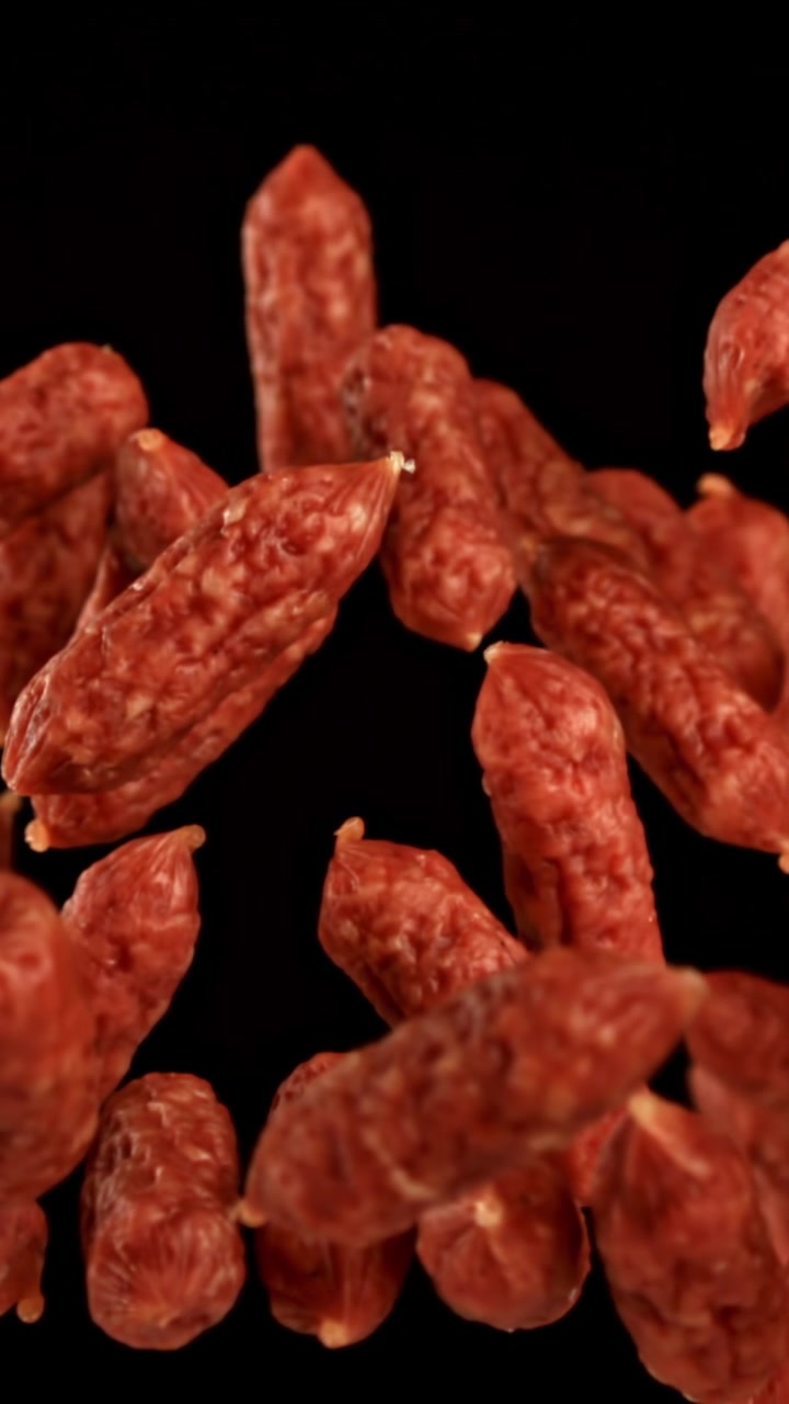 Mini kiełbaski salami spadające i unoszące się na czarnym tle w zwolnionym tempie